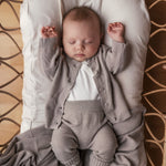 Baby iført beige/grå strikket sæt liggende i flettet kurv med beige tæppe