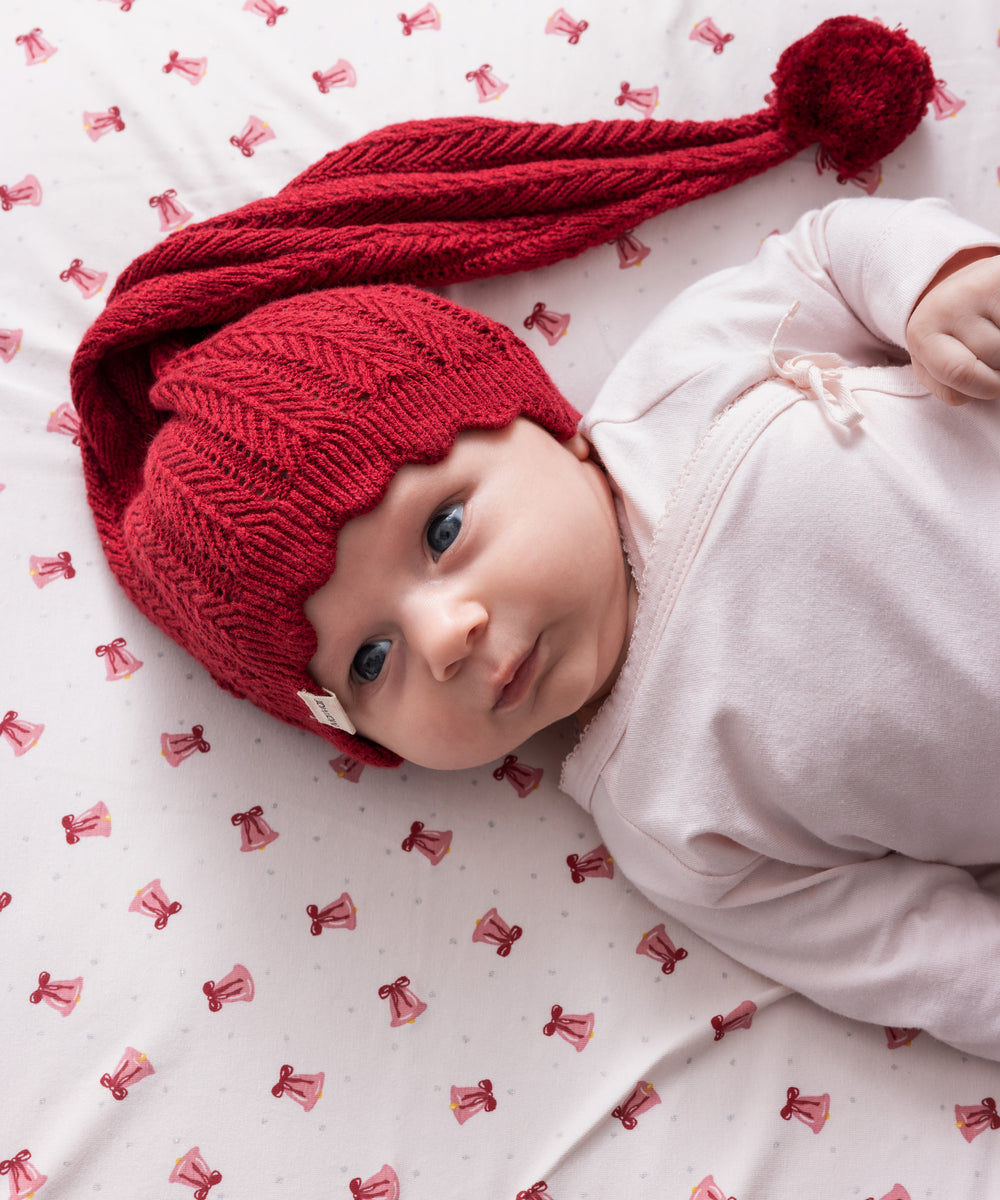 Baby iført rød strikket nissehue med kvast og lyserødt juletøj