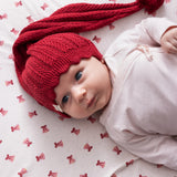 Baby iført rød strikket nissehue med kvast og lyserødt juletøj