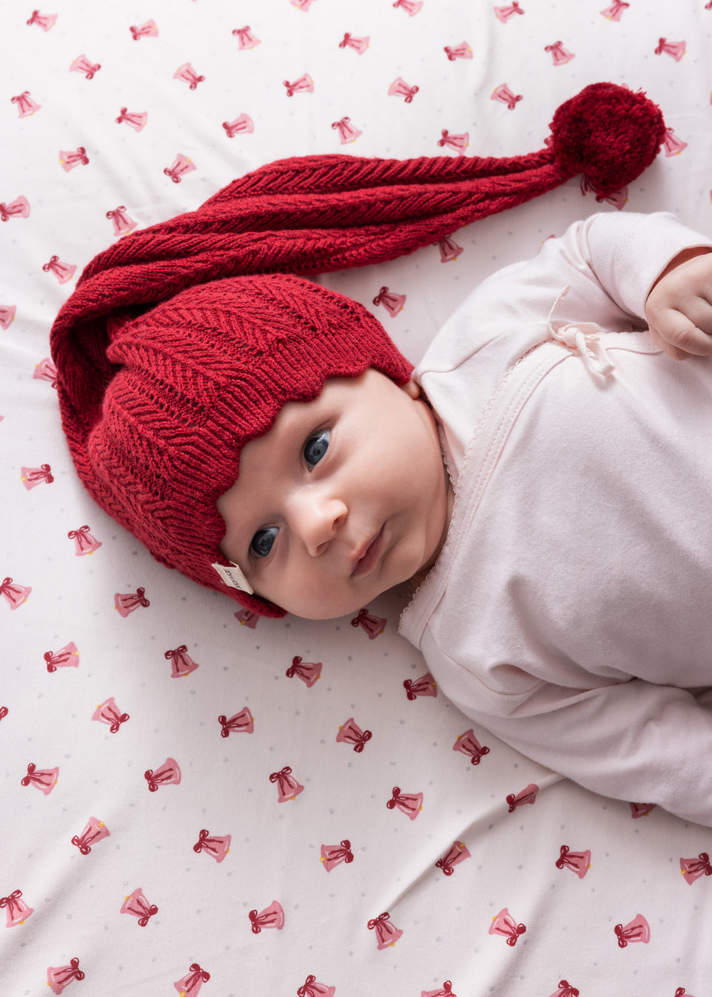 Baby liggende på cremefarvet tæppe med røde juleklokker