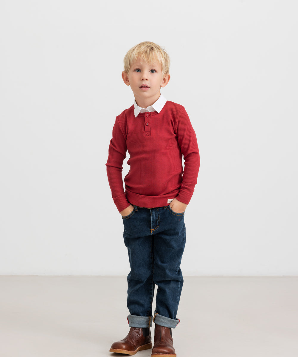 Dreng iført rød ribbluse, hvid skjorte og mørke børnejeans