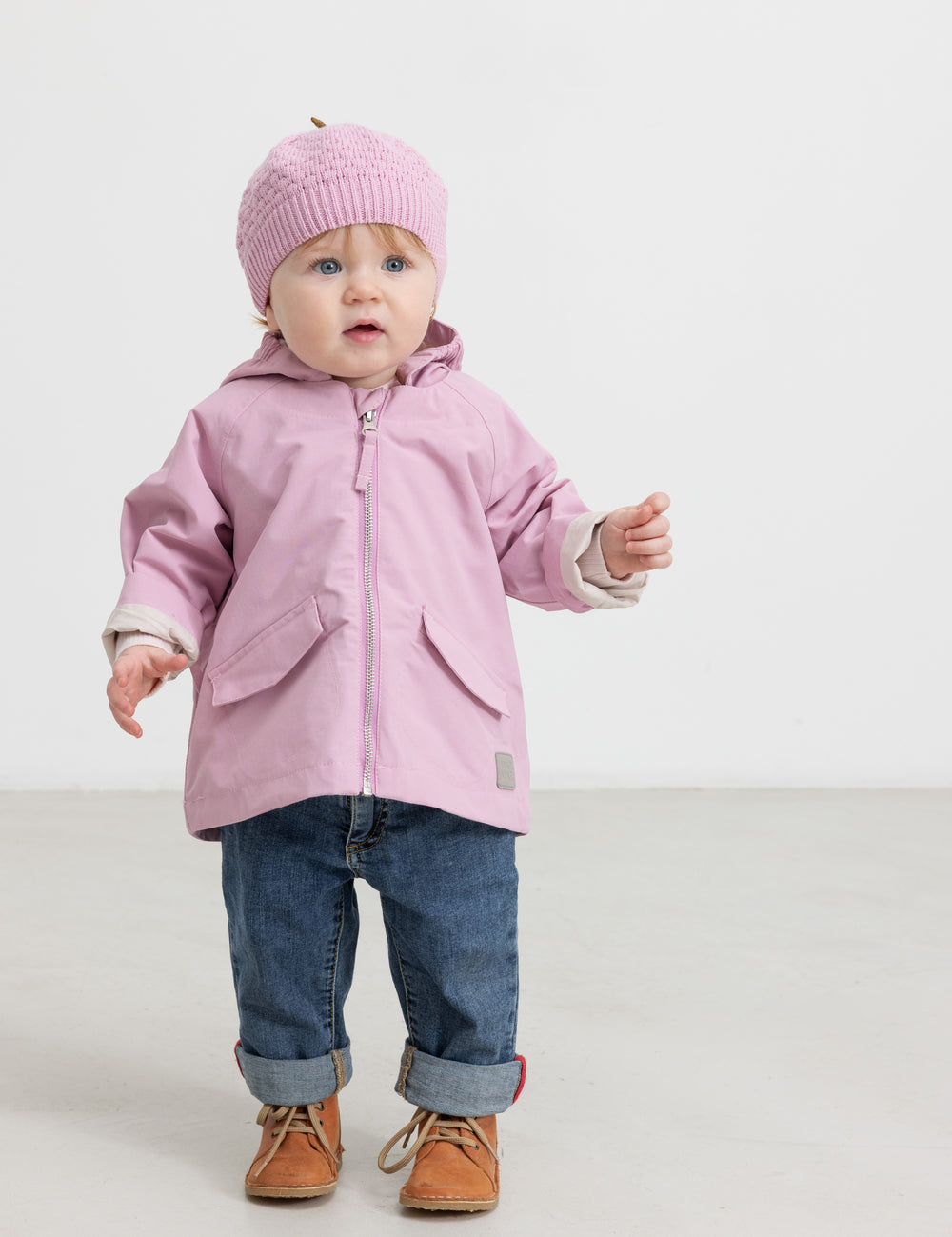 Baby iført lyserød strikket hue og rosa overtøj