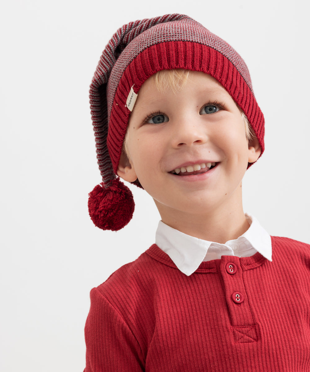 Dreng iført strikket nissehue med røde og grå striber og rød trøje til børn
