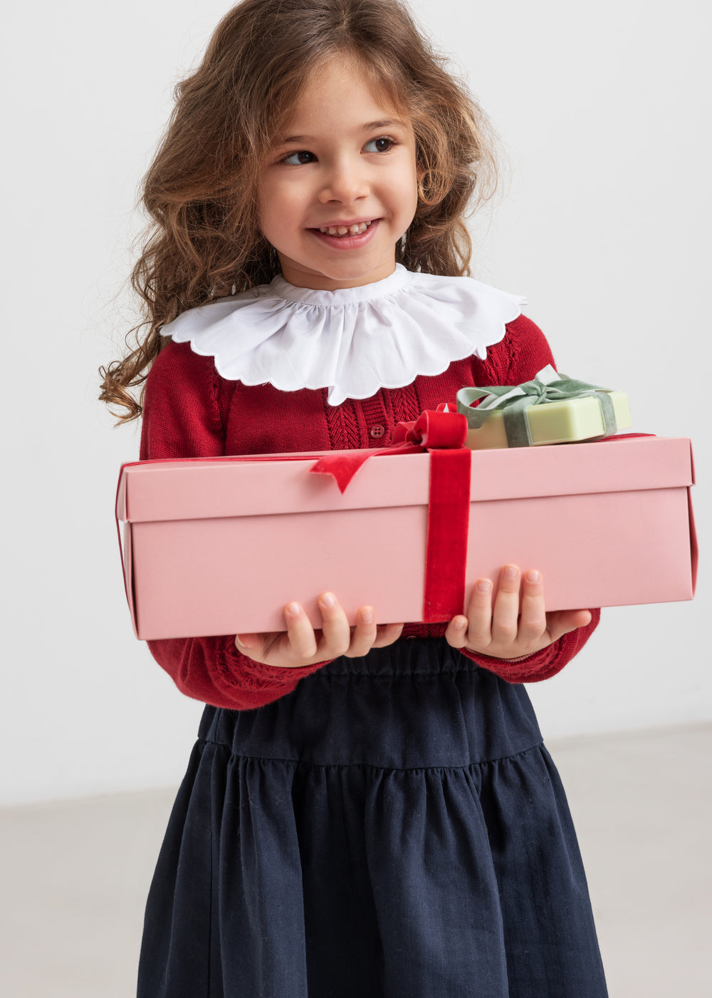 Pige iført rød juletrøje med hulmønster og hvid krave og blå nederdel, holder julegaver