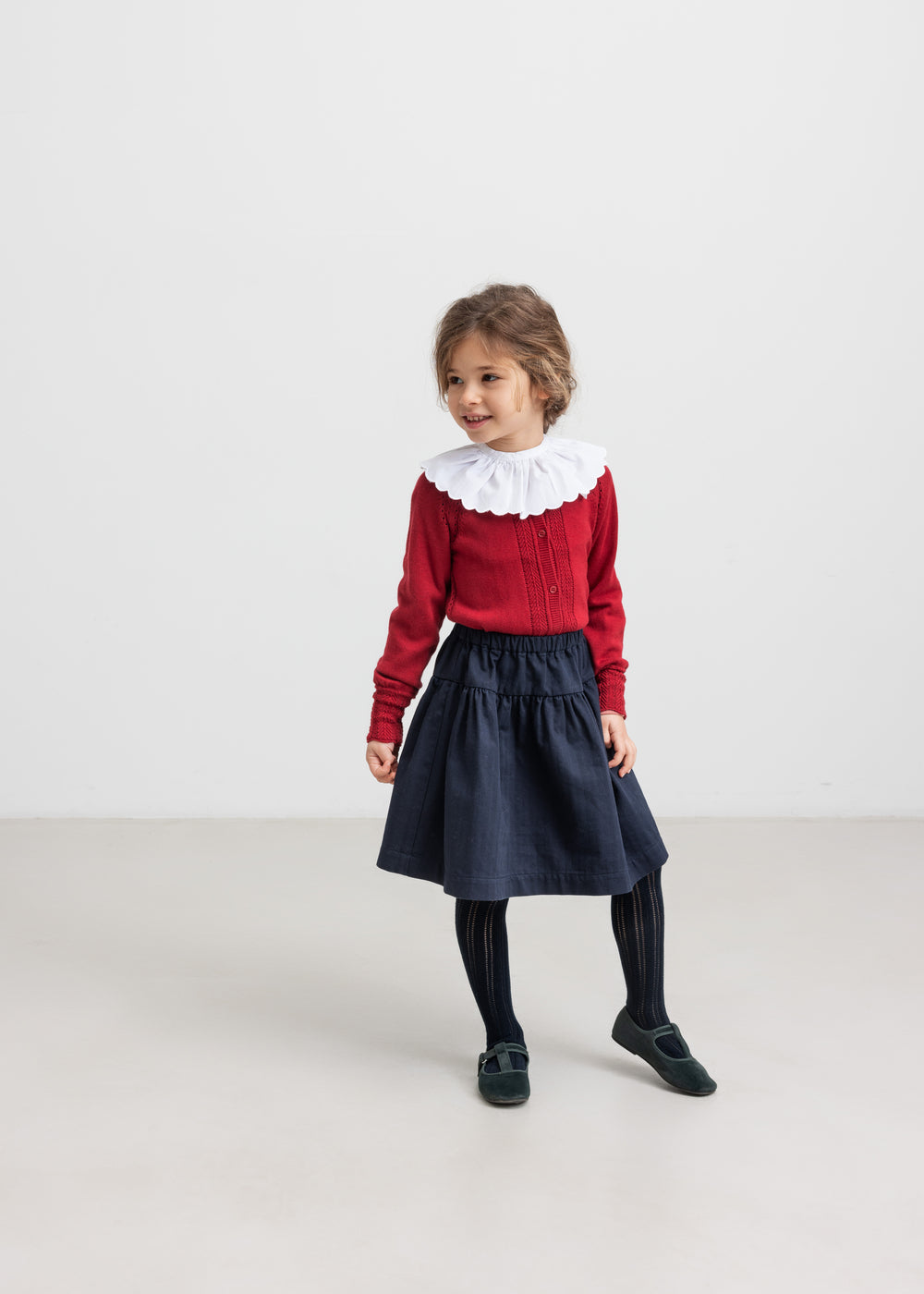 Pige iført mørkeblåt nederdel, rød bluse med hvid krave og sorte strømpebukser til børn