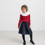 Pige iført mørkeblåt nederdel, rød bluse med hvid krave og sorte strømpebukser til børn