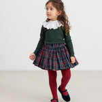 Pige iført juletøj - mørkeblåt og rødt ternet nederdel, mørkegrøn bluse og røde strømpebukser til børn