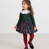 Pige iført mørkegrøn bluse, ternet nederdel og røde strømpebukser – festligt outfit til børn