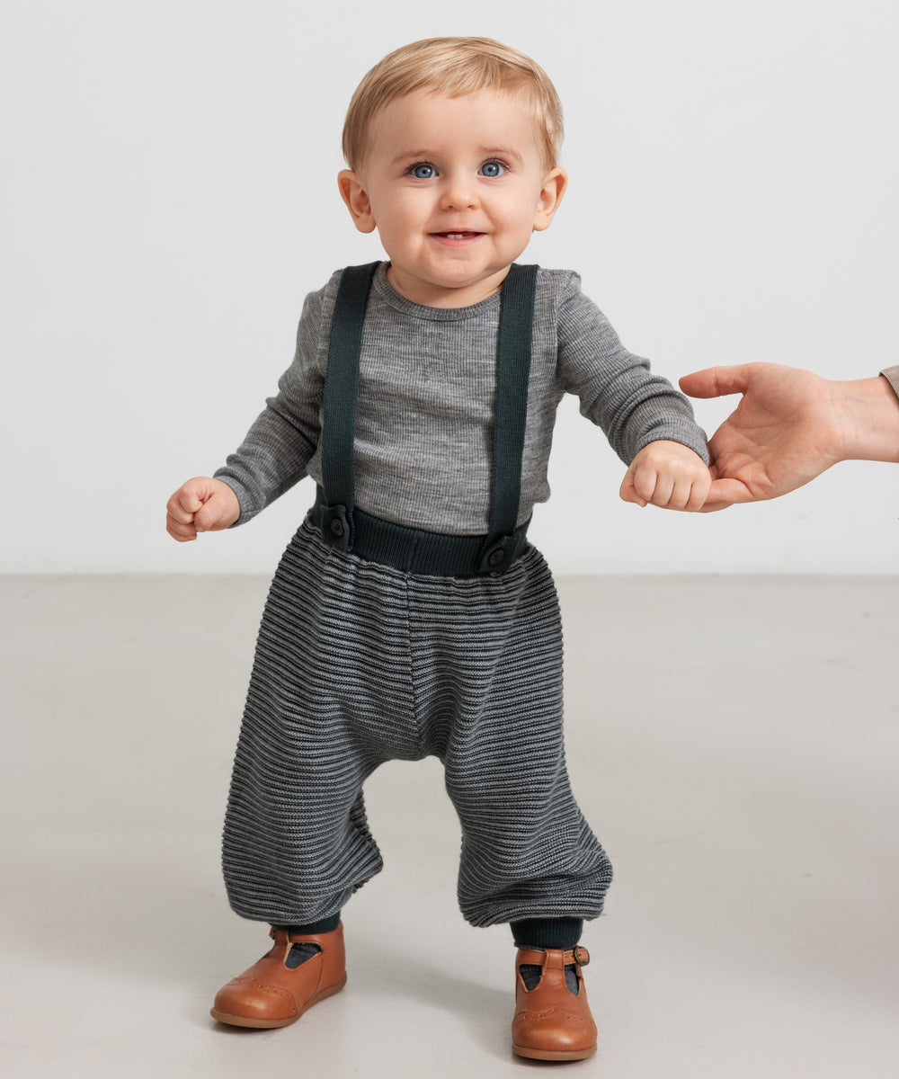 Baby iført mørkegrønne strikkede bukser med seler og grå bluse