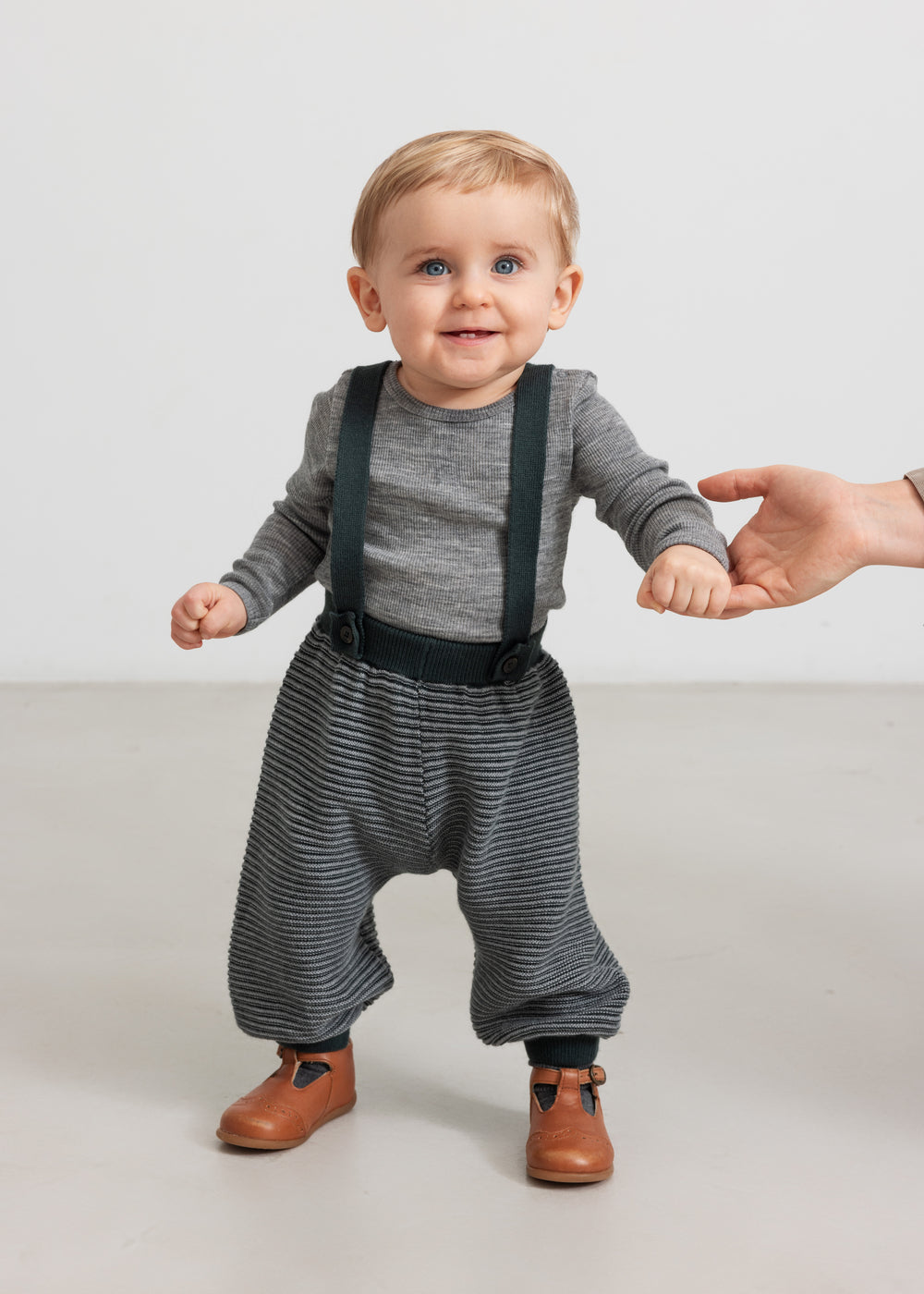 Baby iført mørkegrønne strikkede bukser med seler og grå bluse