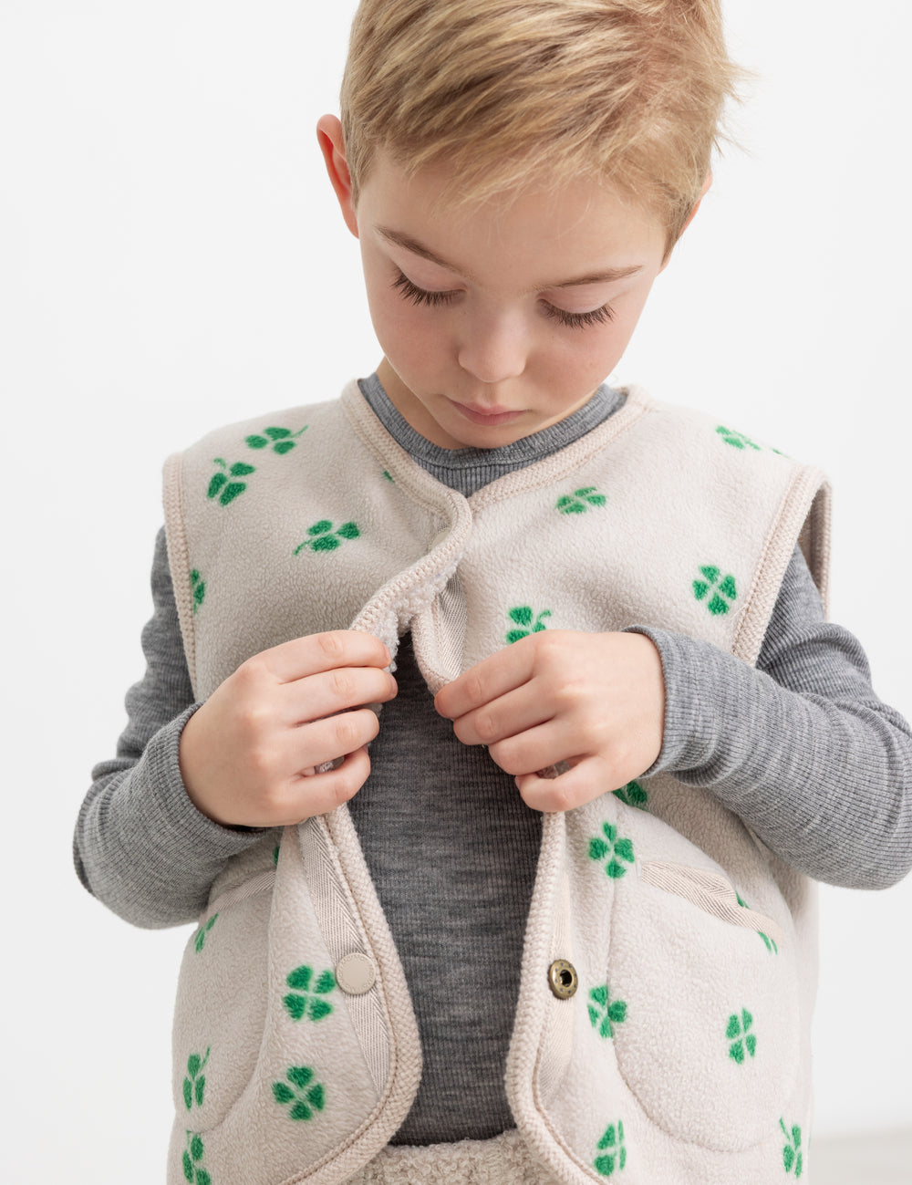 Barn iført beige vest med grønt kløverprint lukket foran