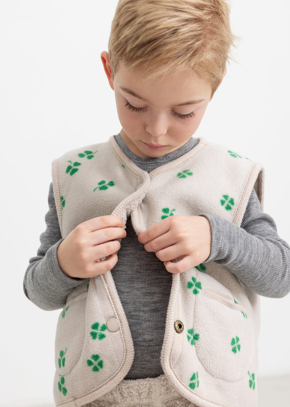 Barn iført beige vest med grønt kløverprint lukket foran