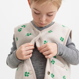 Barn iført beige vest med grønt kløverprint lukket foran
