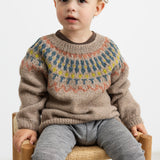 Dreng iført beige uldstrikbluse med mønster sidder på stol