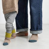 Barn iført uldstrømper i beige med grøn rib, orange hæl og blå tå