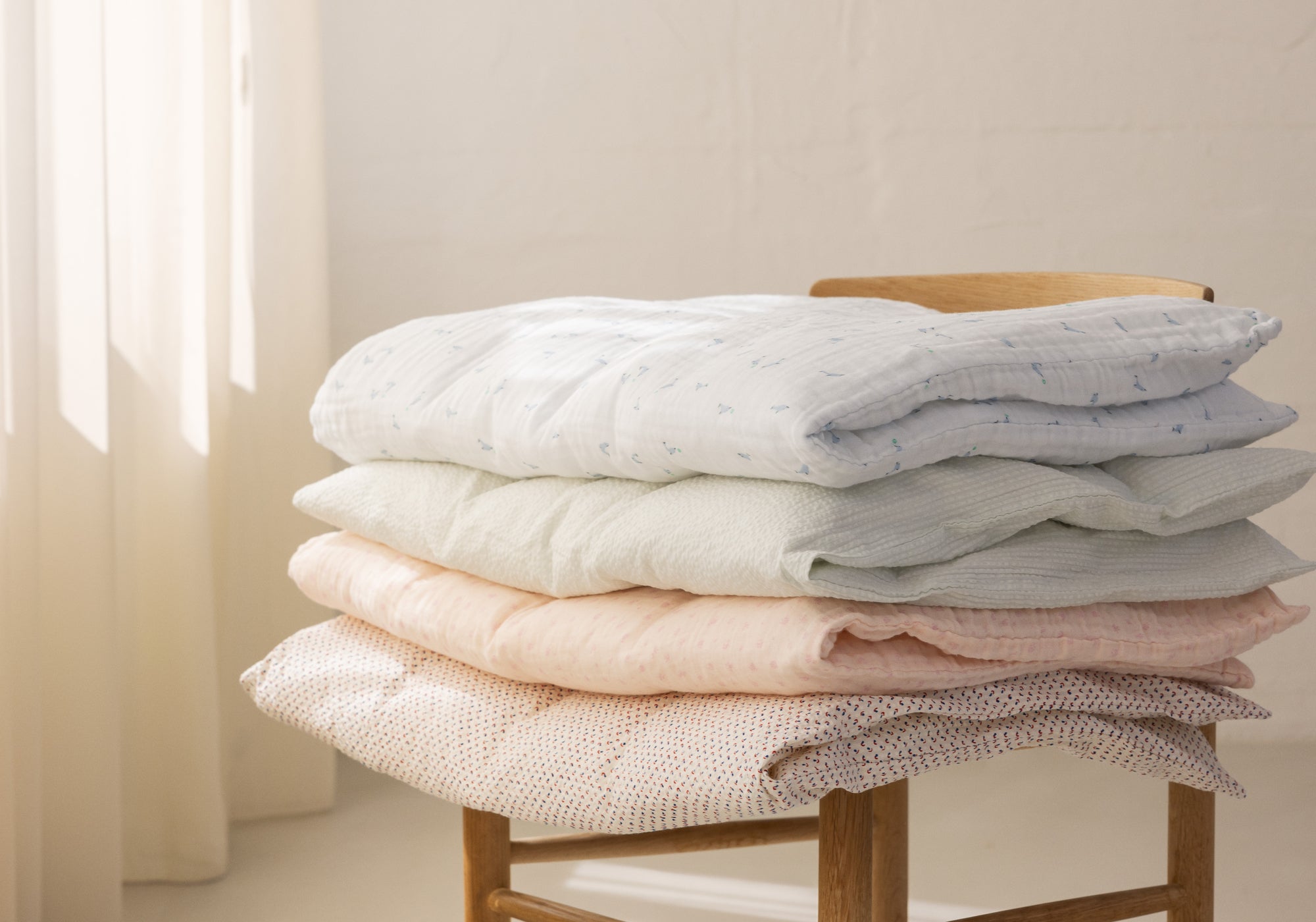 Stable af blødt sengetøj i lyse nuancer på en stol