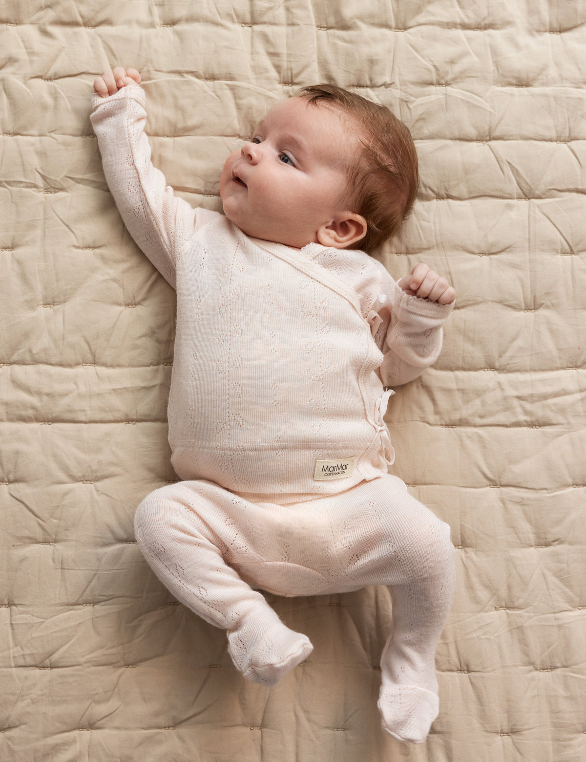 Nyfødt baby i lyserød pointelle-body og bukser liggende på quiltet tæppe