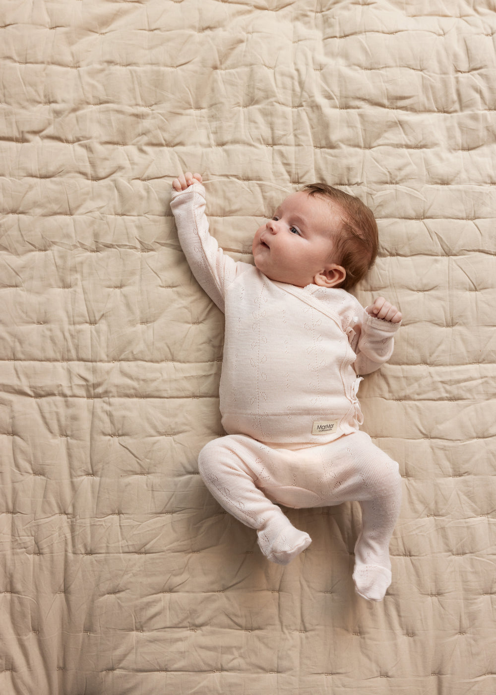 Baby iført lyserød heldragt i merinould ligger på tæppe