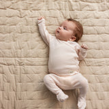 Baby iført lyserød heldragt i merinould ligger på tæppe