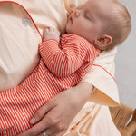 Baby iført rød og hvid stribet heldragt sover i favnen på en voksen