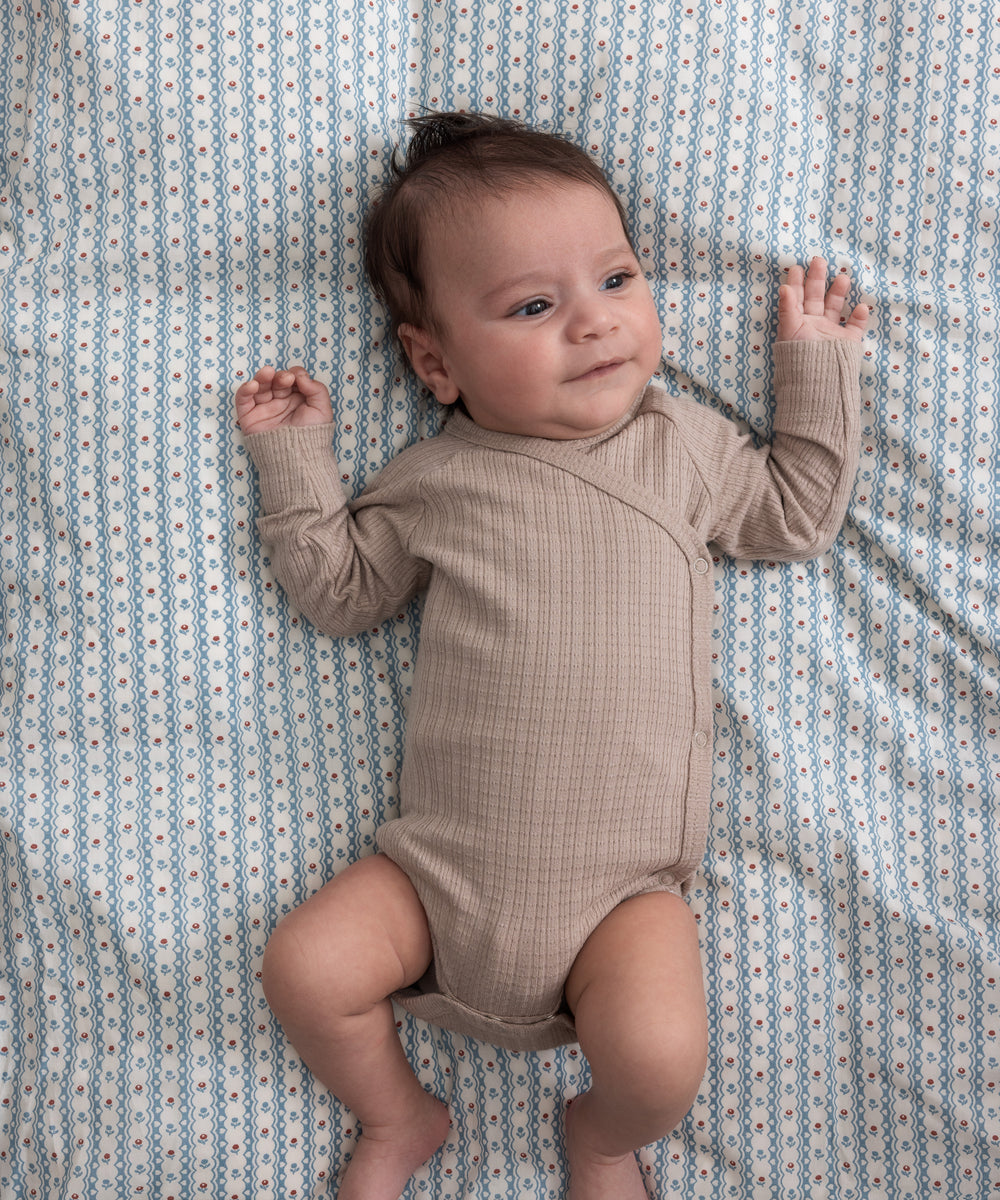 Børn iført beige pointelle slå-om body liggende på et blåt mønstret tæppe