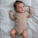 Børn iført beige pointelle slå-om body liggende på et blåt mønstret tæppe