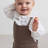 barn iført brune selebukser og hvid bluse