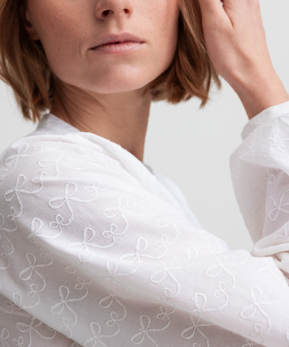 Kvinde iført hvid skjortebluse med broderet mønster