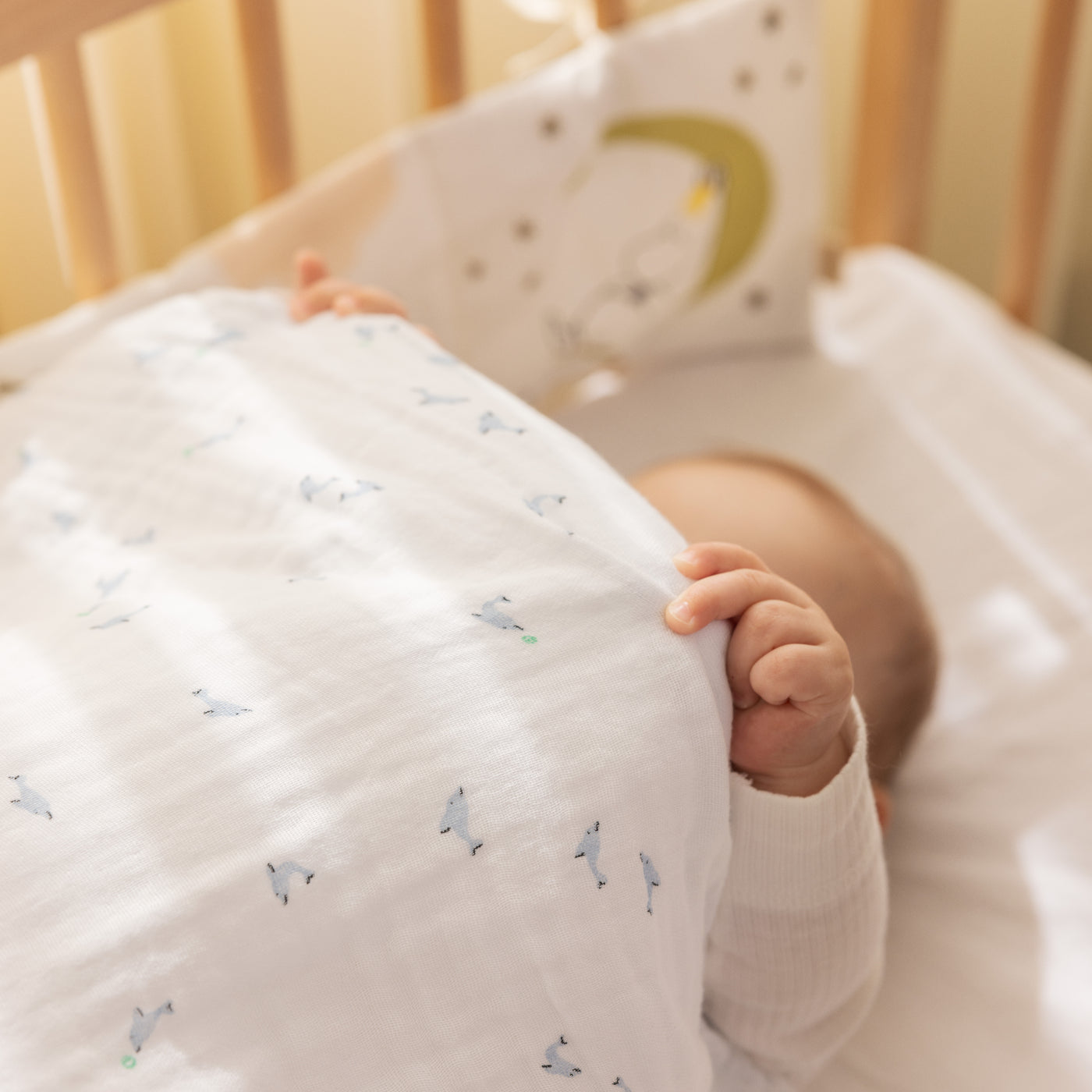 Baby ligger i tremmeseng under blødt sengetøj med små blå valer print