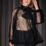 Kvinde iført sort tylbluse med sløjfe og sorte bukser