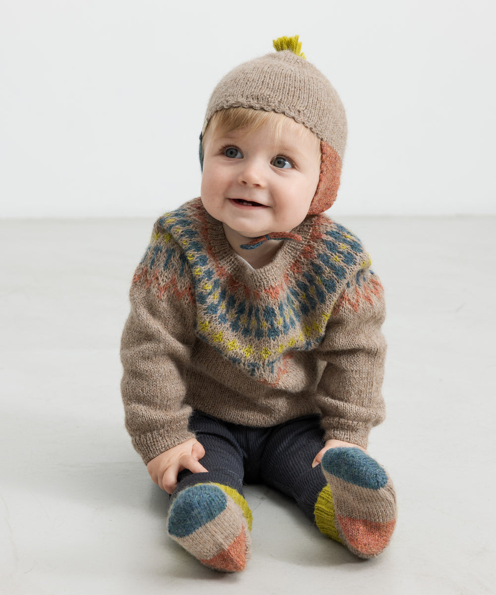 Baby iført beige uldhue med kvast og strikket trøje