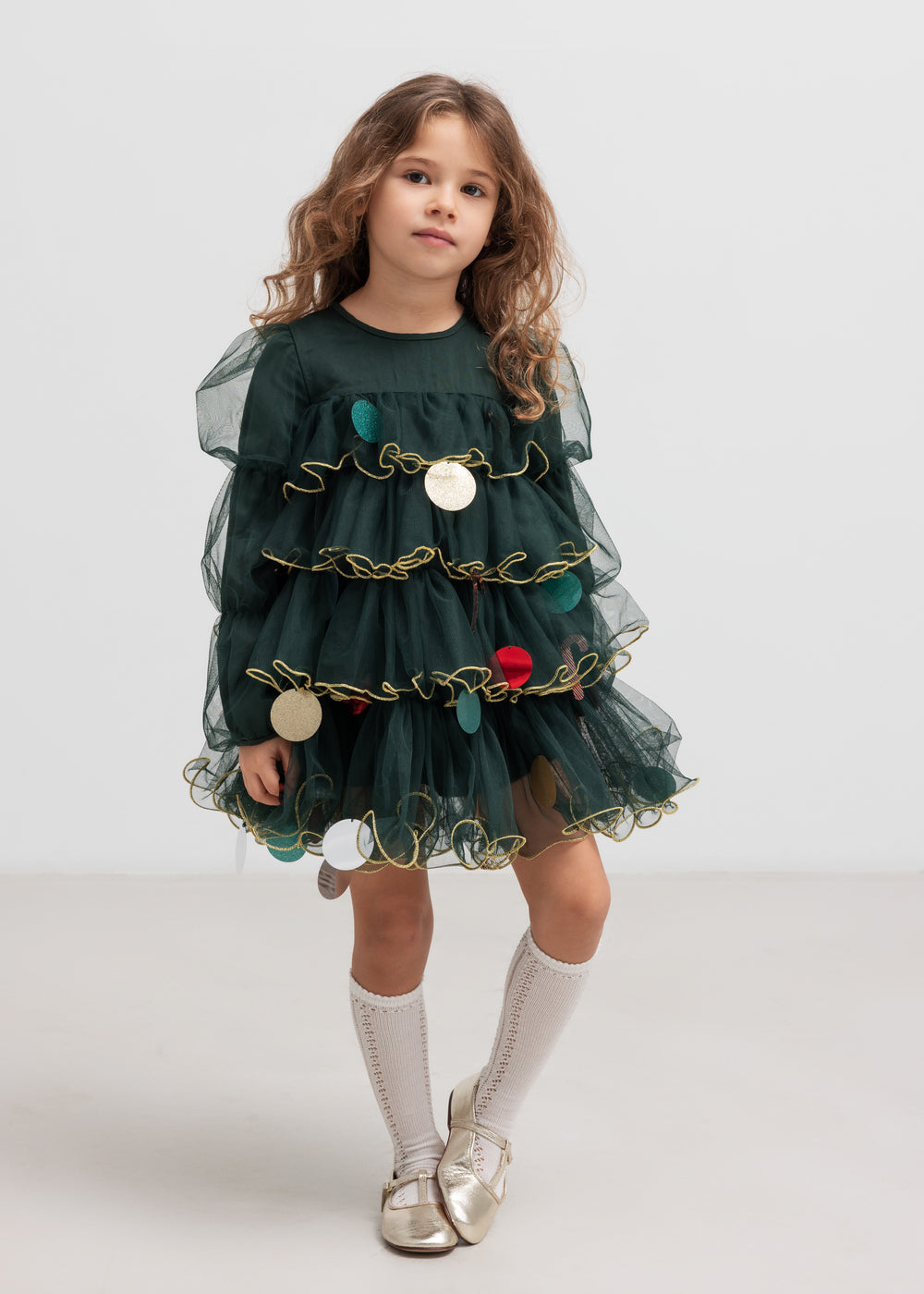 Pige iført mørkegrøn julekjole i tyl med guldkanter og juledetaljer til børn