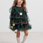 Pige iført mørkegrøn julekjole i tyl med guldkanter og juledetaljer til børn