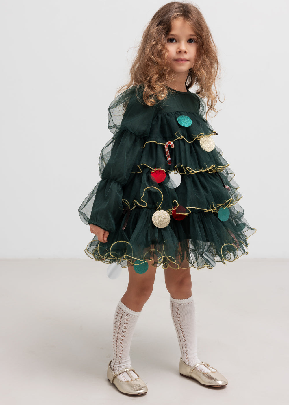 Pige iført mørkegrøn julekjole i tyl med guldkanter og juledetaljer til børn