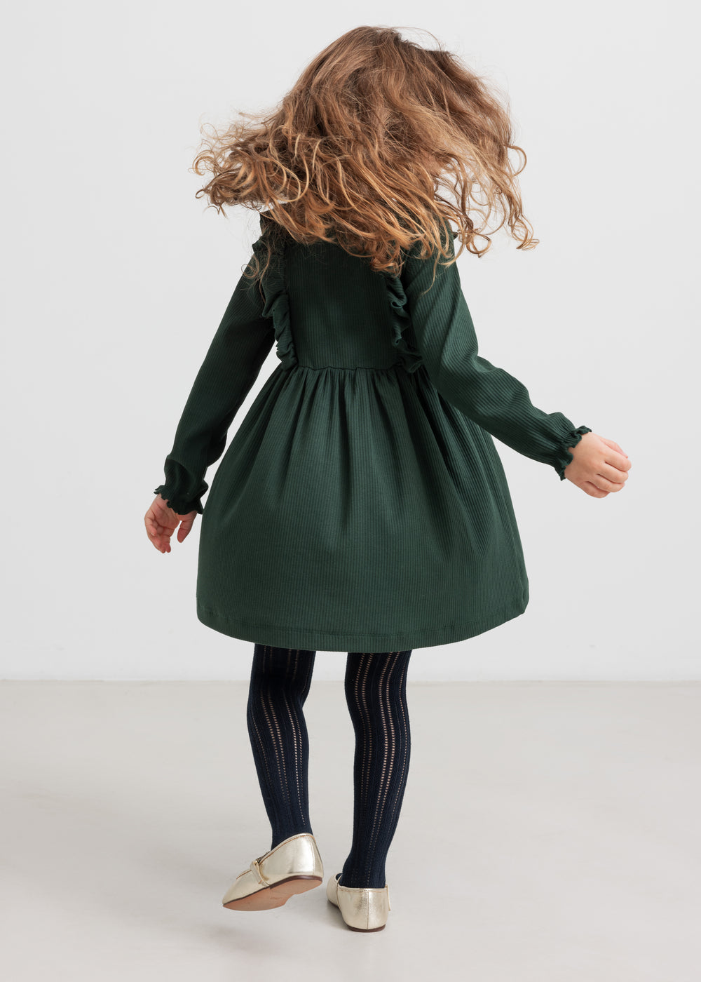 Pige iført grøn ribstrikket julekjole med flæser på skuldrene