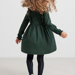 Pige iført grøn ribstrikket julekjole med flæser på skuldrene