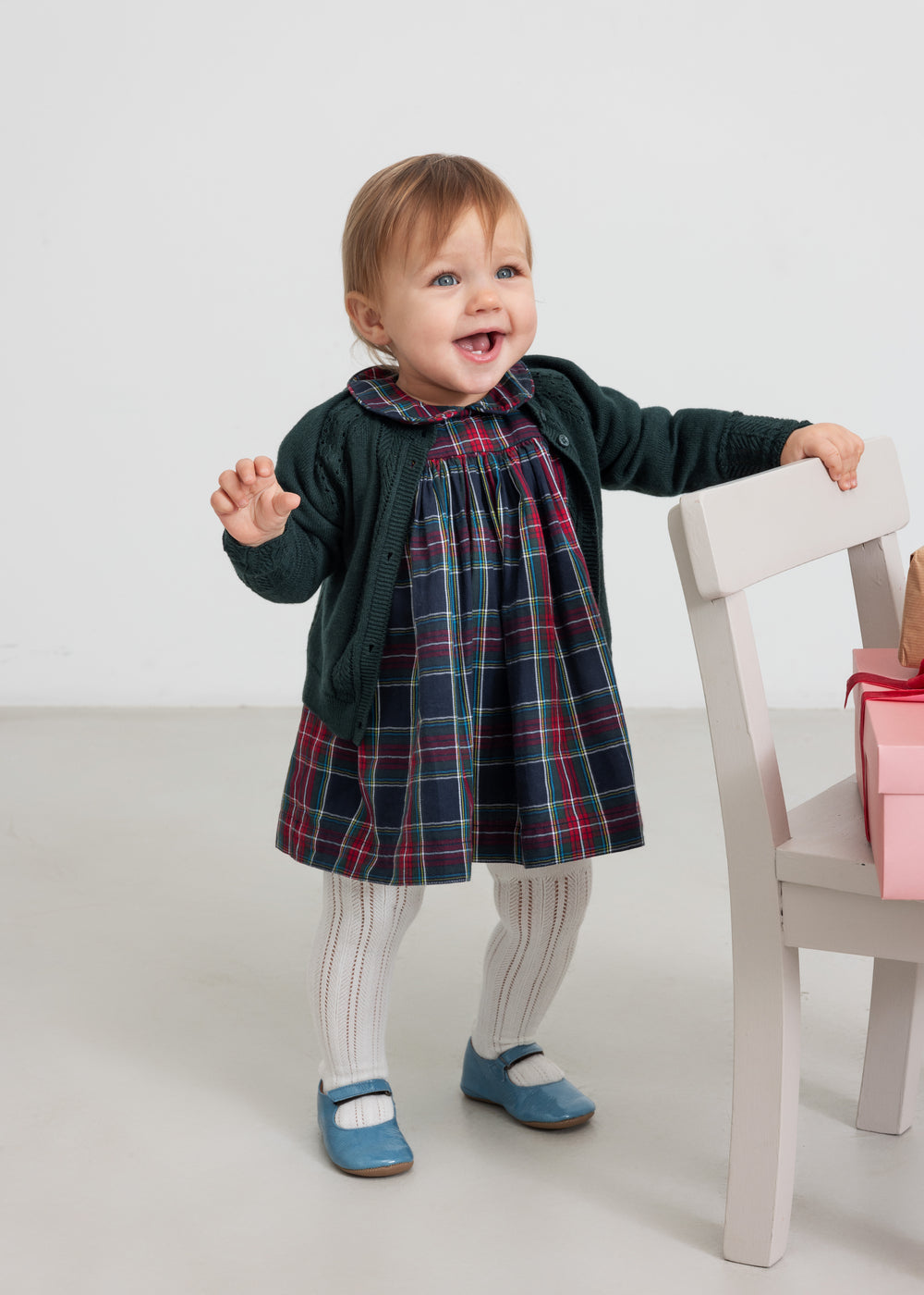 Baby iført mørkegrøn cardigan med hulmønster og ternet rød og grøn julekjole