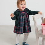 Baby iført mørkegrøn cardigan med hulmønster og ternet rød og grøn julekjole