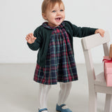 Baby iført mørkegrøn cardigan med hulmønster og ternet rød og grøn julekjole