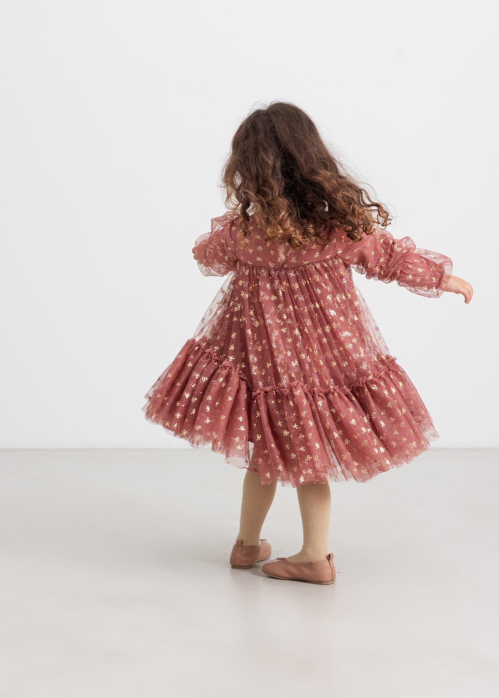 Pige iført rosa festkjole i tyl med guldprint og flæser til børn