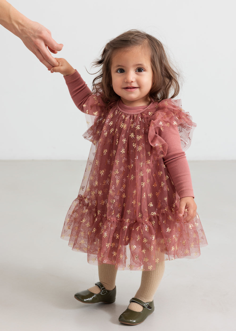 Baby iført rosa festlig kjole i tyl med flæser og gyldne detaljer