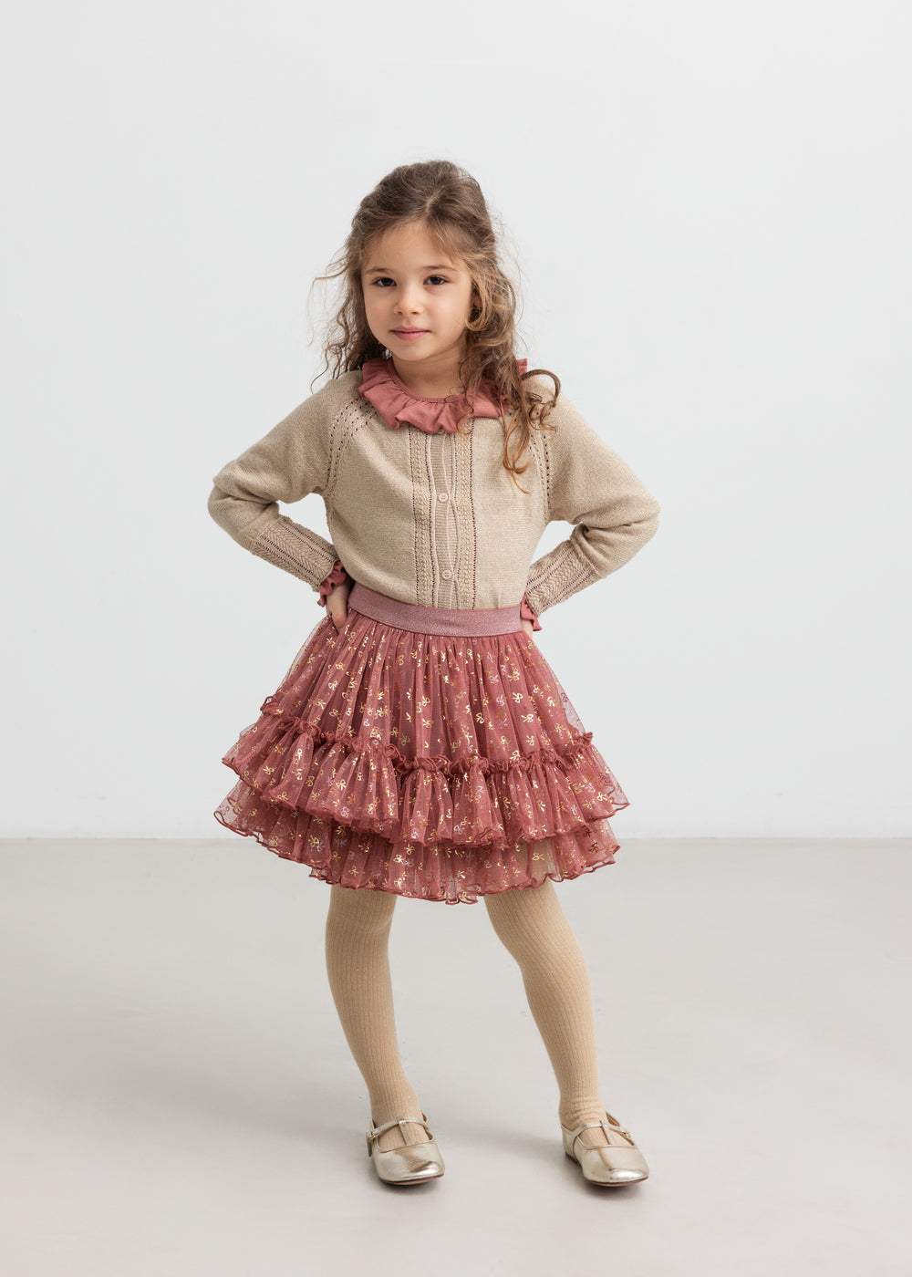 Pige iført rosa tylnederdel med guldprint, beige cardigan og strømpebukser til børn