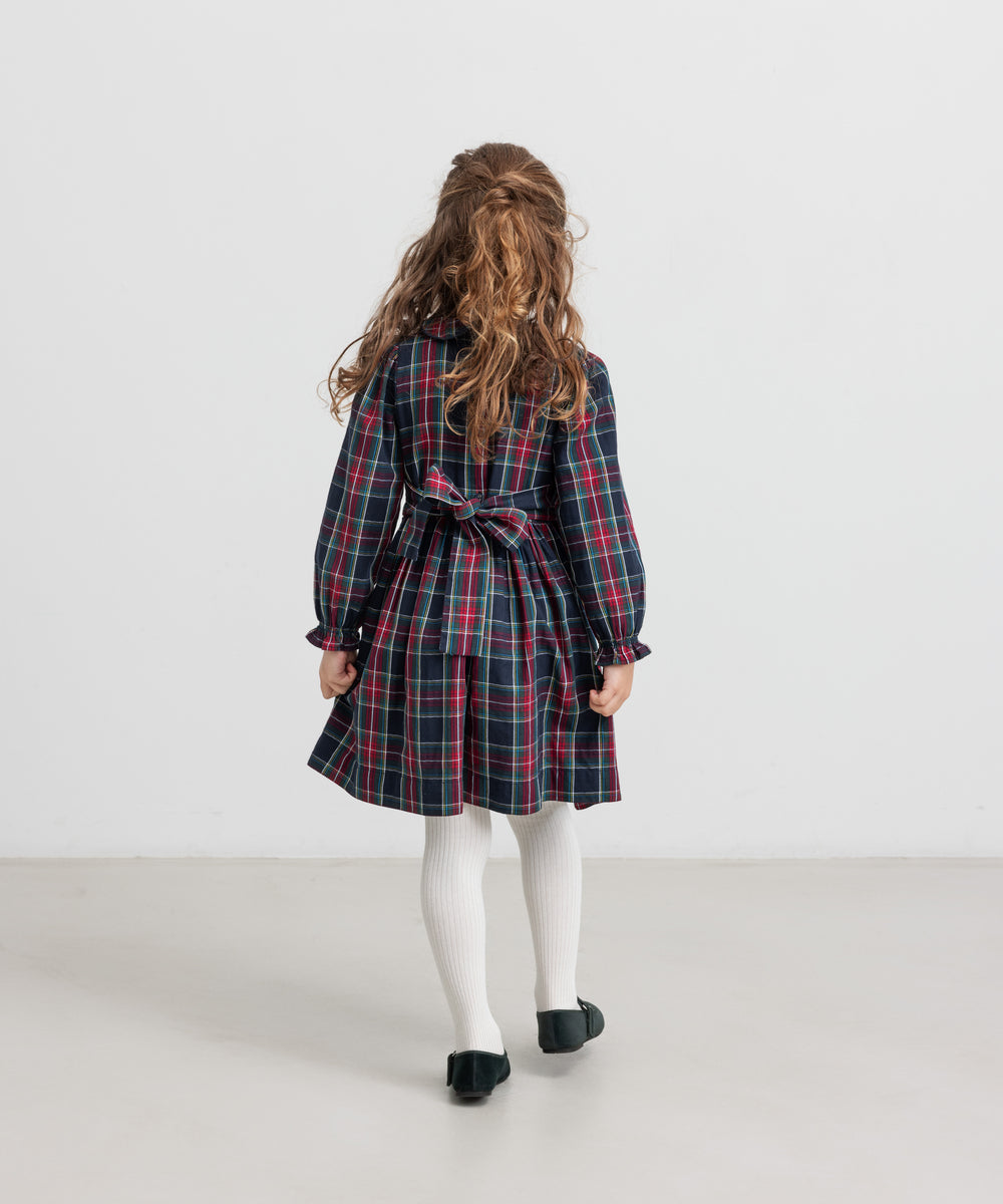 Pige iført mørkeblå og rød ternet julekjole med krave og hvide strømpebukser til børn