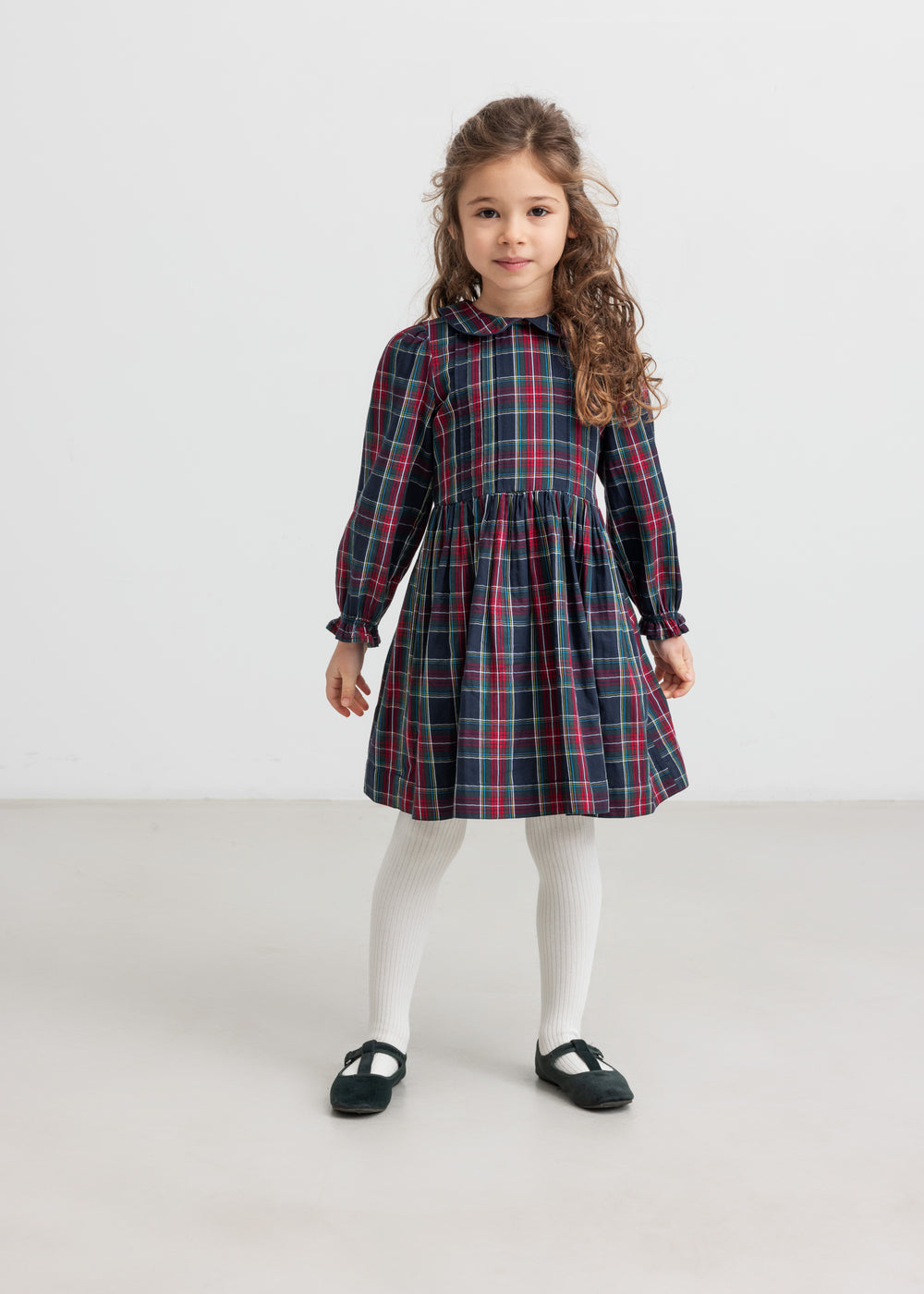 Pige iført mørkeblå og rød ternet julekjole med krave og hvide strømpebukser til børn