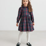 Pige iført mørkeblå og rød ternet julekjole med krave og hvide strømpebukser til børn