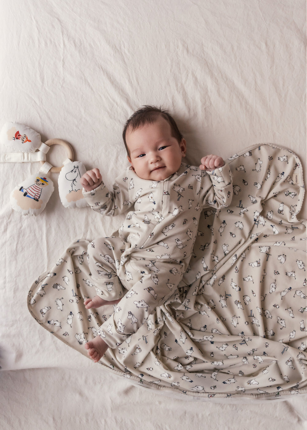 Baby iført heldragt med lange ærmer, trykknapper og Moomin-tryk i lyse farver