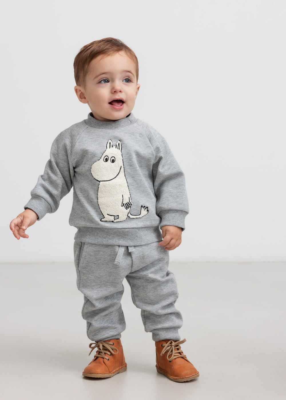 Lille børn iført grå sweatshirt med Moomin print og grå joggingbukser