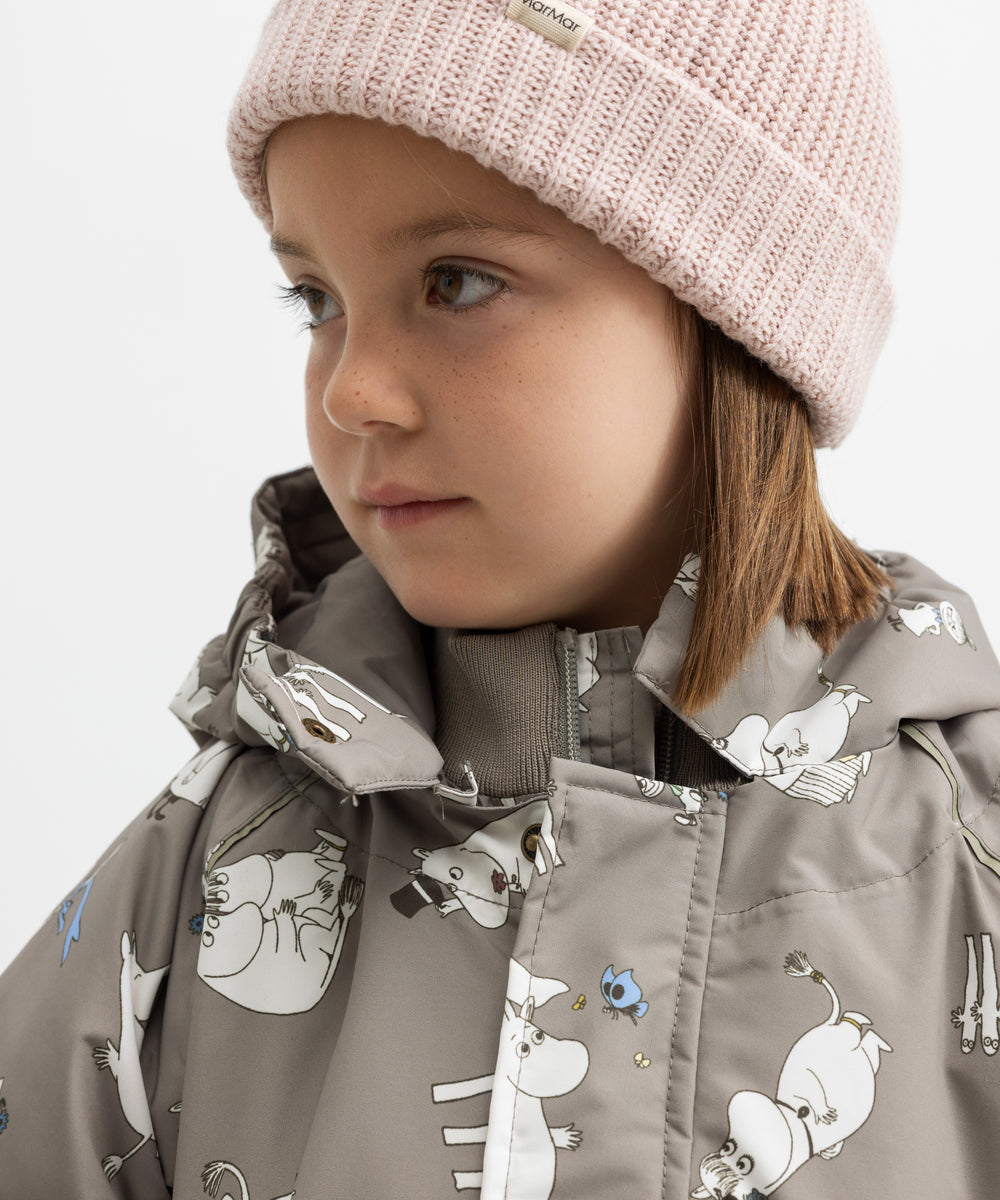 Barn iført lyserød strikhue og beige jakke med Moomin print
