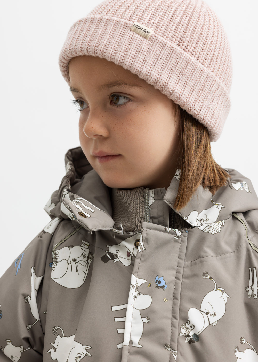 Barn iført lyserød strikhue og beige jakke med Moomin print