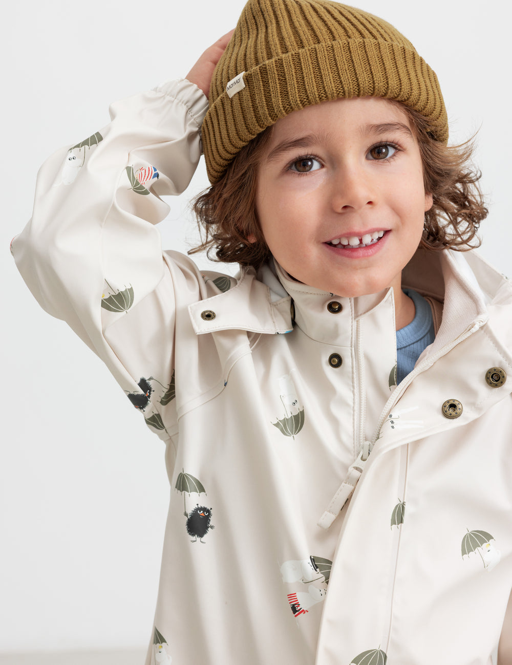 Barn iført beige regnjakke med Moomin print og strikket hue